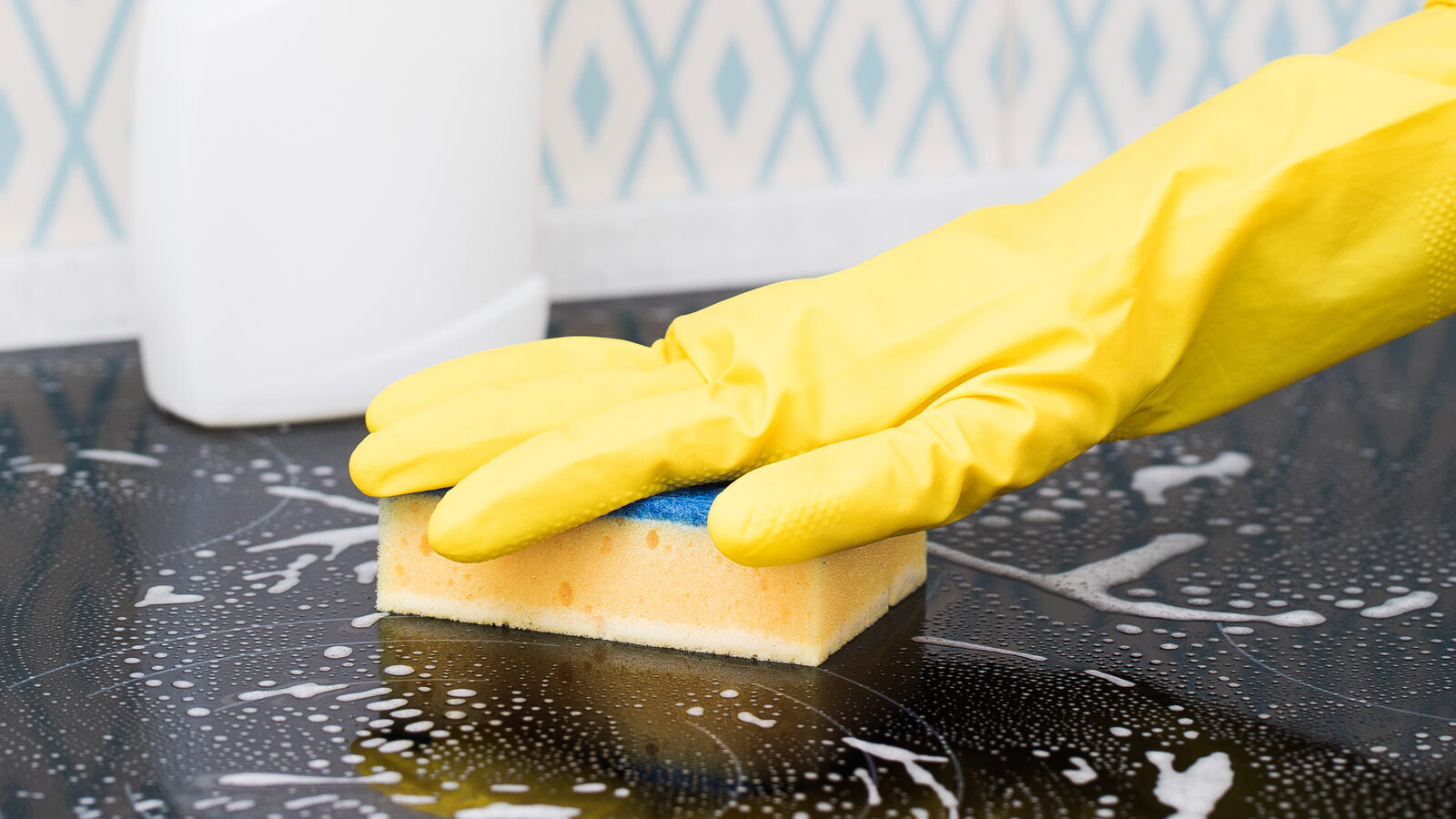 A gloved hand wiping down a kitchen counter with a sponge.